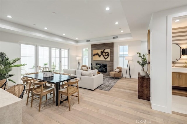 dining area featuring a large fireplace, a tray ceiling, light wood-type flooring, and a healthy amount of sunlight