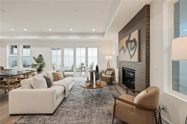 living room featuring recessed lighting, a raised ceiling, wood finished floors, and a glass covered fireplace