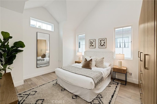 bedroom featuring high vaulted ceiling, baseboards, and light wood finished floors