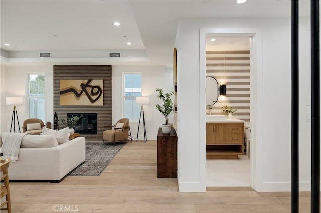 living room featuring a large fireplace, a tray ceiling, light wood finished floors, and visible vents