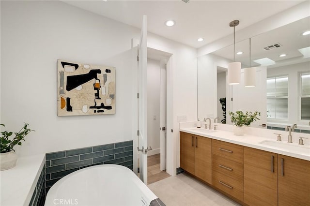 bathroom featuring double vanity, a freestanding tub, visible vents, and a sink