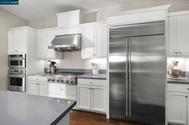 kitchen featuring white cabinetry, stainless steel appliances, wall chimney range hood, and dark hardwood / wood-style flooring