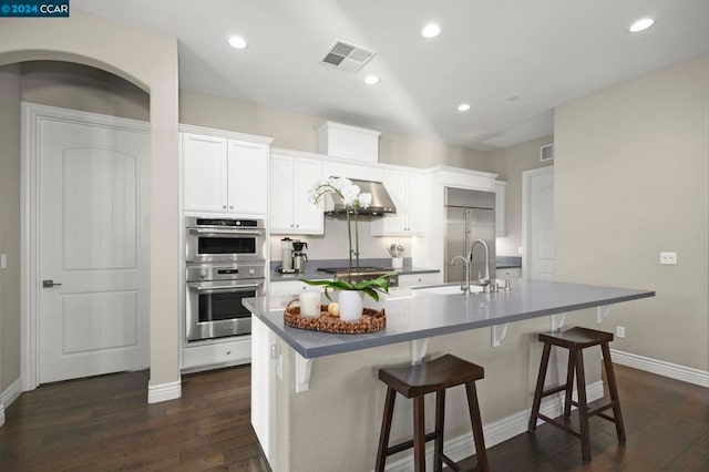 kitchen featuring white cabinetry, stainless steel appliances, a center island with sink, and dark hardwood / wood-style floors