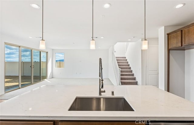 kitchen with open floor plan, pendant lighting, light stone counters, recessed lighting, and a sink