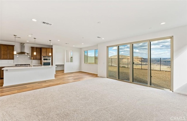 unfurnished living room with visible vents, recessed lighting, light colored carpet, and light wood-type flooring