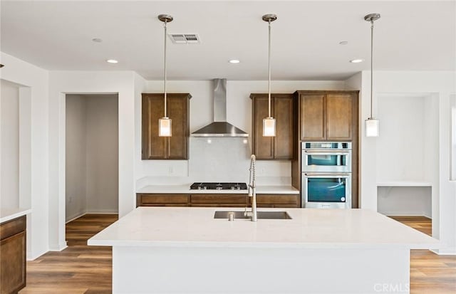 kitchen featuring visible vents, wall chimney range hood, gas cooktop, double oven, and light wood finished floors