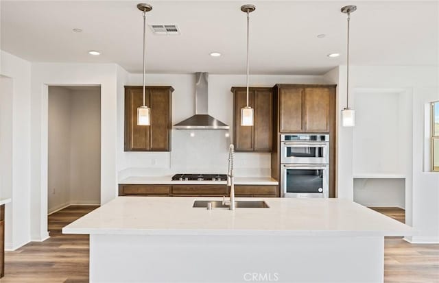 kitchen with visible vents, light wood-style flooring, stainless steel double oven, gas stovetop, and wall chimney exhaust hood