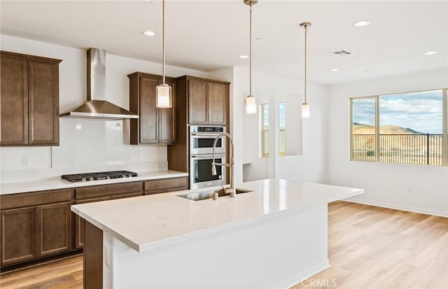 kitchen featuring a sink, wall chimney range hood, gas cooktop, double oven, and light wood finished floors