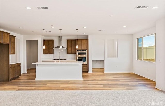 kitchen with visible vents, double oven, light countertops, and wall chimney exhaust hood