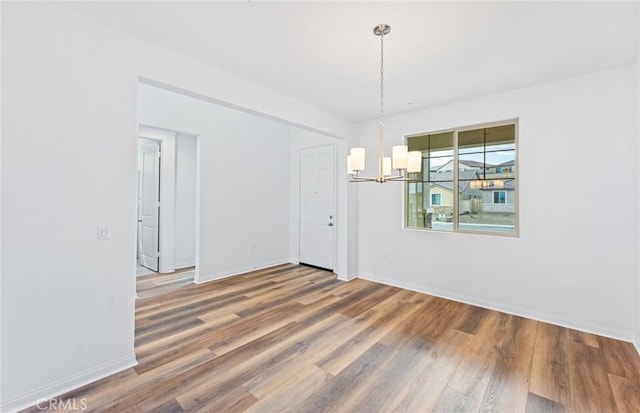 unfurnished dining area with a chandelier, baseboards, and wood finished floors