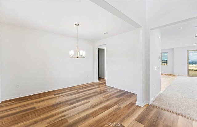 spare room with light wood-style flooring, baseboards, and an inviting chandelier