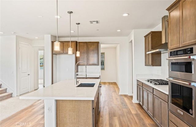 kitchen featuring visible vents, a sink, stainless steel appliances, light wood-style floors, and wall chimney exhaust hood