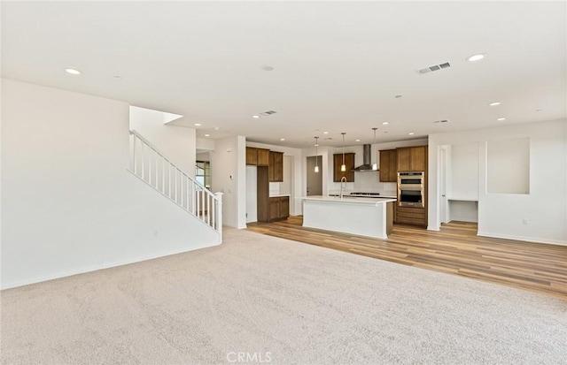 unfurnished living room featuring light wood-type flooring, recessed lighting, stairway, baseboards, and light colored carpet