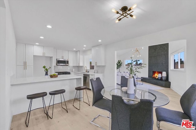 dining space featuring a notable chandelier, light wood-type flooring, sink, and a tile fireplace