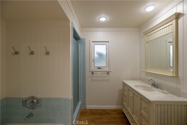 bathroom with wood-type flooring, vanity, crown molding, and a tile shower