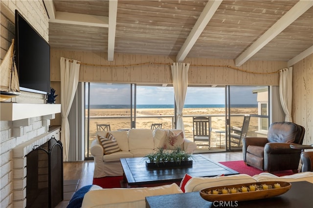 living room with lofted ceiling with beams, wood ceiling, a brick fireplace, a water view, and hardwood / wood-style floors