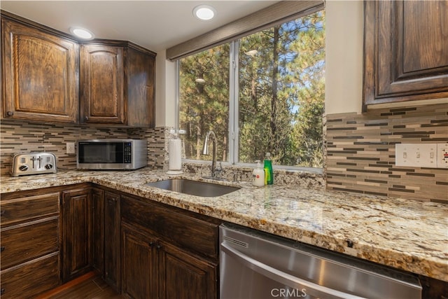 kitchen with light stone counters, sink, decorative backsplash, stainless steel appliances, and dark brown cabinetry