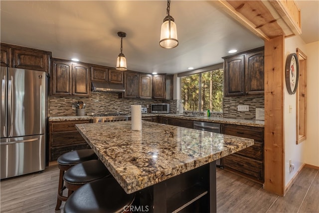 kitchen featuring dark wood-type flooring, dark brown cabinetry, appliances with stainless steel finishes, and a kitchen island