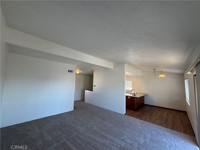 empty room featuring dark carpet, a healthy amount of sunlight, a sink, and visible vents