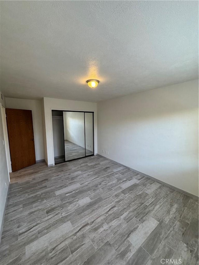 unfurnished bedroom with a textured ceiling, a closet, and wood finished floors