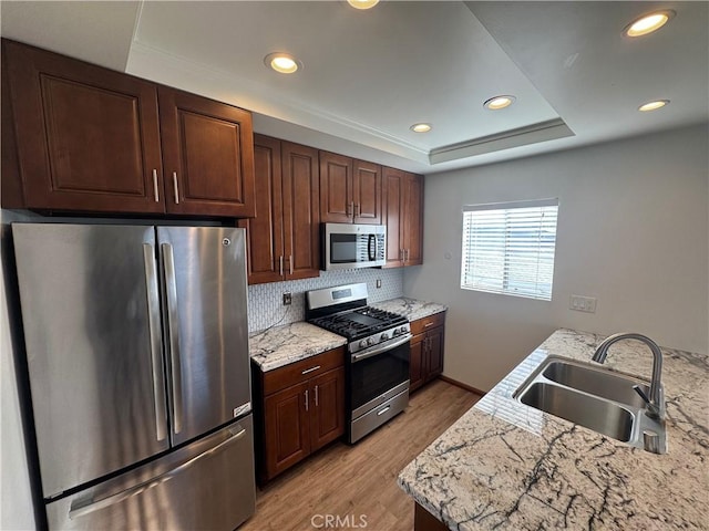 kitchen with a raised ceiling, appliances with stainless steel finishes, light countertops, light wood-type flooring, and a sink