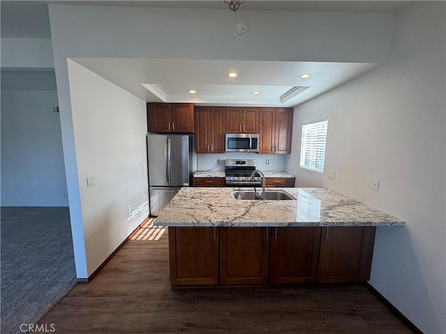 kitchen featuring a raised ceiling, backsplash, appliances with stainless steel finishes, a sink, and light stone countertops