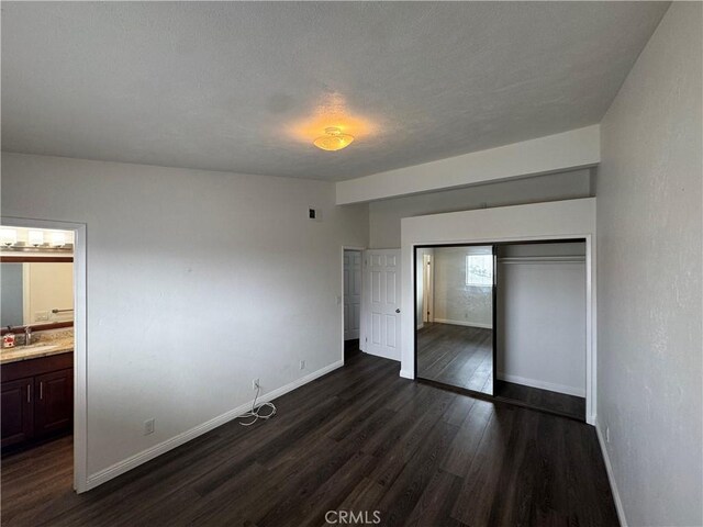 unfurnished bedroom featuring a closet, baseboards, connected bathroom, dark wood-style flooring, and a sink