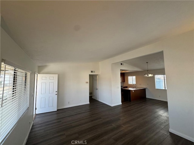 unfurnished living room with baseboards, a chandelier, dark wood finished floors, and a sink