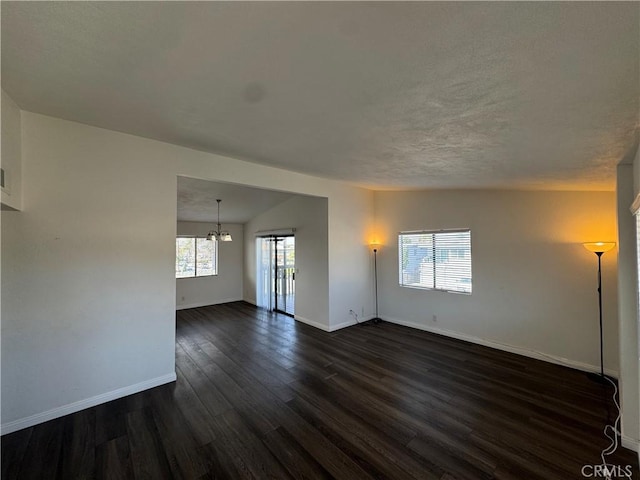 unfurnished room with a chandelier, a textured ceiling, dark wood finished floors, and baseboards