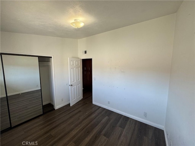 unfurnished bedroom featuring visible vents, a closet, baseboards, and dark wood-type flooring