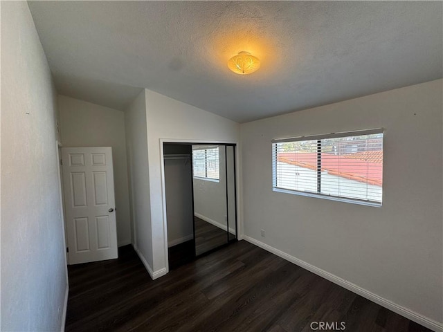 unfurnished bedroom featuring dark wood finished floors, a closet, vaulted ceiling, a textured ceiling, and baseboards