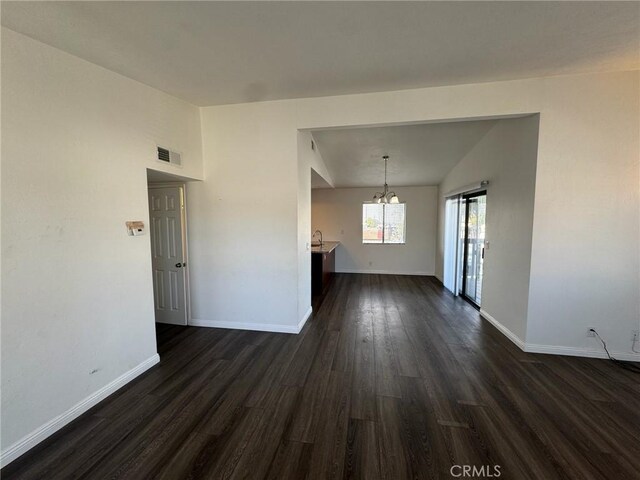 spare room with dark wood-style floors, lofted ceiling, visible vents, a chandelier, and baseboards