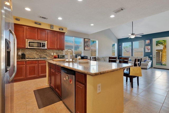 kitchen featuring sink, vaulted ceiling, light tile patterned floors, an island with sink, and appliances with stainless steel finishes