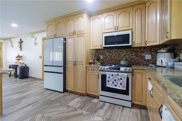 kitchen with light stone countertops, light brown cabinetry, stainless steel gas stove, and white fridge