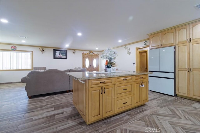 kitchen with white fridge, light brown cabinetry, ornamental molding, light stone counters, and a center island