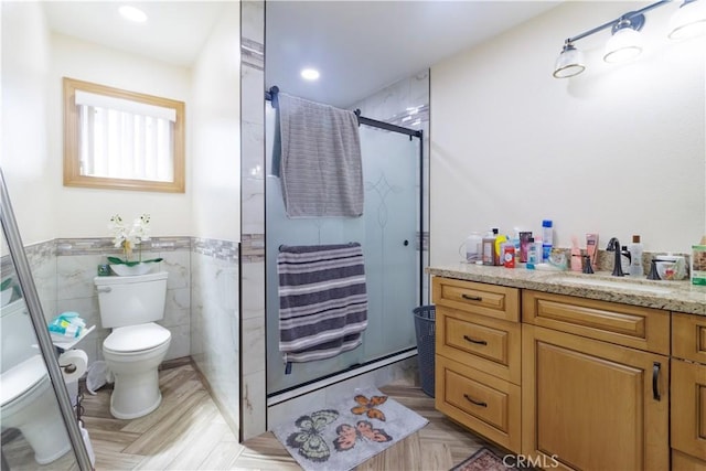 bathroom featuring toilet, vanity, tile walls, and a shower with door