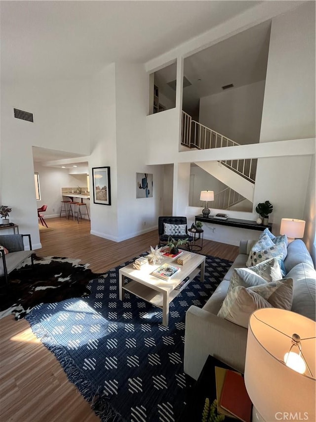 living room featuring wood finished floors, high vaulted ceiling, visible vents, and stairs