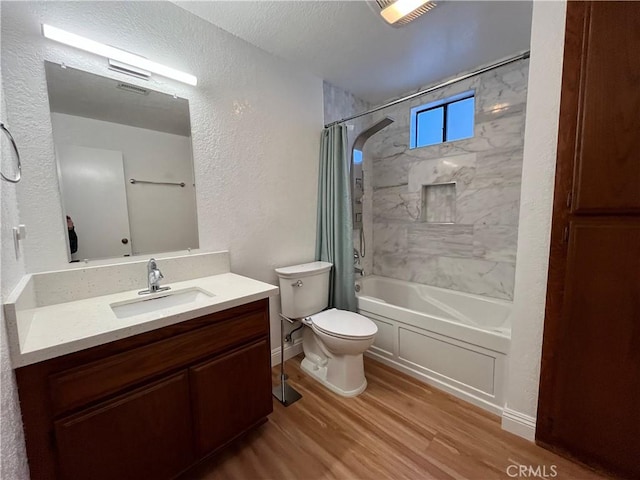 full bathroom with toilet, a textured wall, shower / bathtub combination with curtain, vanity, and wood finished floors