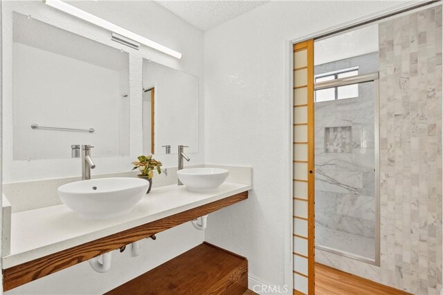 full bath featuring a sink, a tile shower, wood finished floors, and a textured ceiling