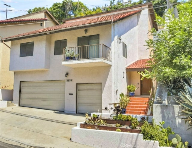 mediterranean / spanish home featuring a tiled roof, a balcony, stucco siding, an attached garage, and driveway