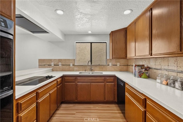 kitchen featuring light countertops, black appliances, decorative backsplash, and a sink