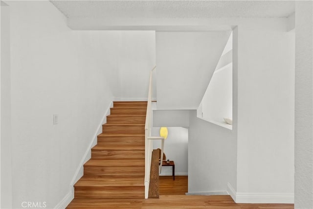 stairway featuring baseboards, a textured ceiling, and wood finished floors