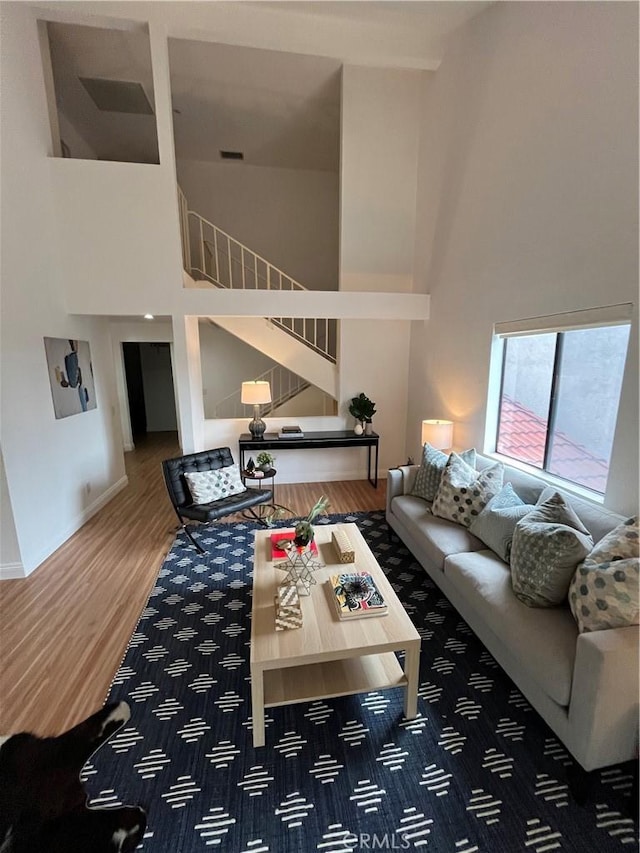 living area featuring stairway, a towering ceiling, wood finished floors, visible vents, and baseboards