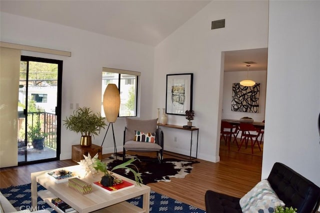 sitting room with high vaulted ceiling, visible vents, baseboards, and wood finished floors