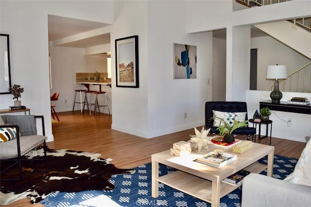 living room featuring stairway, a towering ceiling, baseboards, and wood finished floors