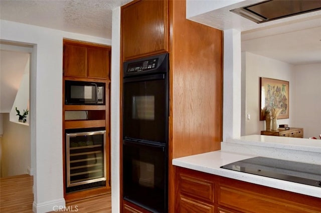 kitchen featuring light countertops, brown cabinetry, black appliances, light wood-style flooring, and beverage cooler
