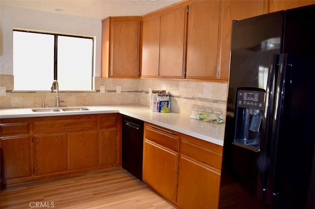 kitchen featuring tasteful backsplash, light countertops, black appliances, brown cabinetry, and a sink