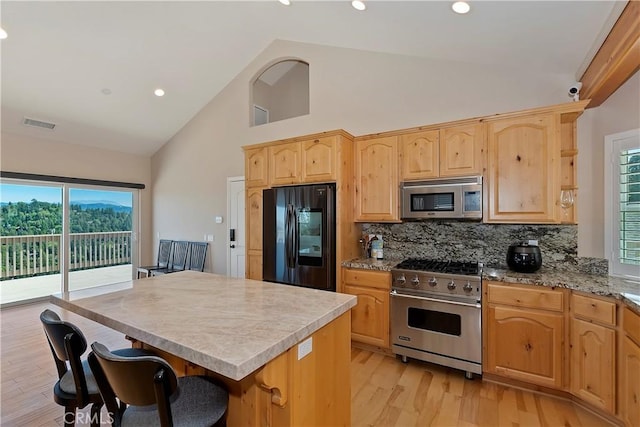 kitchen featuring appliances with stainless steel finishes, backsplash, high vaulted ceiling, a center island, and light hardwood / wood-style floors