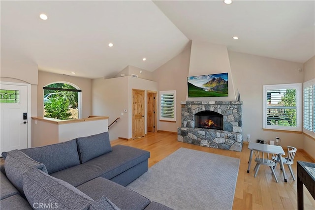 living room featuring high vaulted ceiling, a fireplace, a wealth of natural light, and light hardwood / wood-style flooring