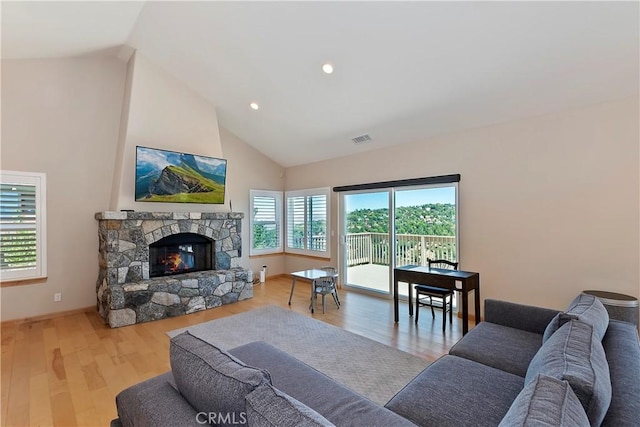 living room with a healthy amount of sunlight, light hardwood / wood-style floors, a fireplace, and high vaulted ceiling